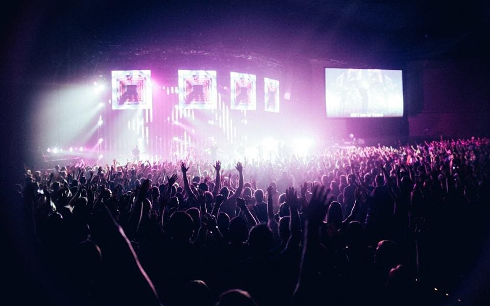 A crowd with raised hands under purple stage lights
