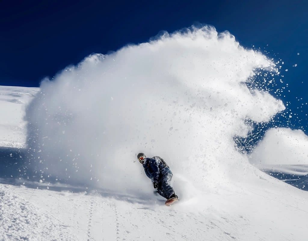 A snowboarder carving through deep powder
