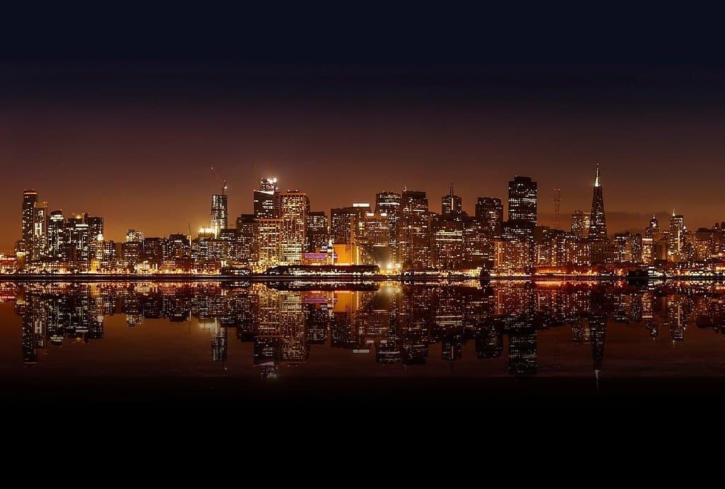 A city skyline at night reflected in the water